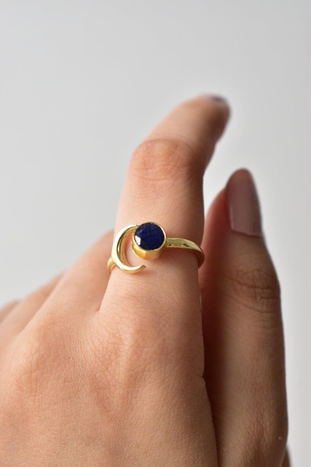 Gold ring with a blue gemstone on a finger against a neutral background