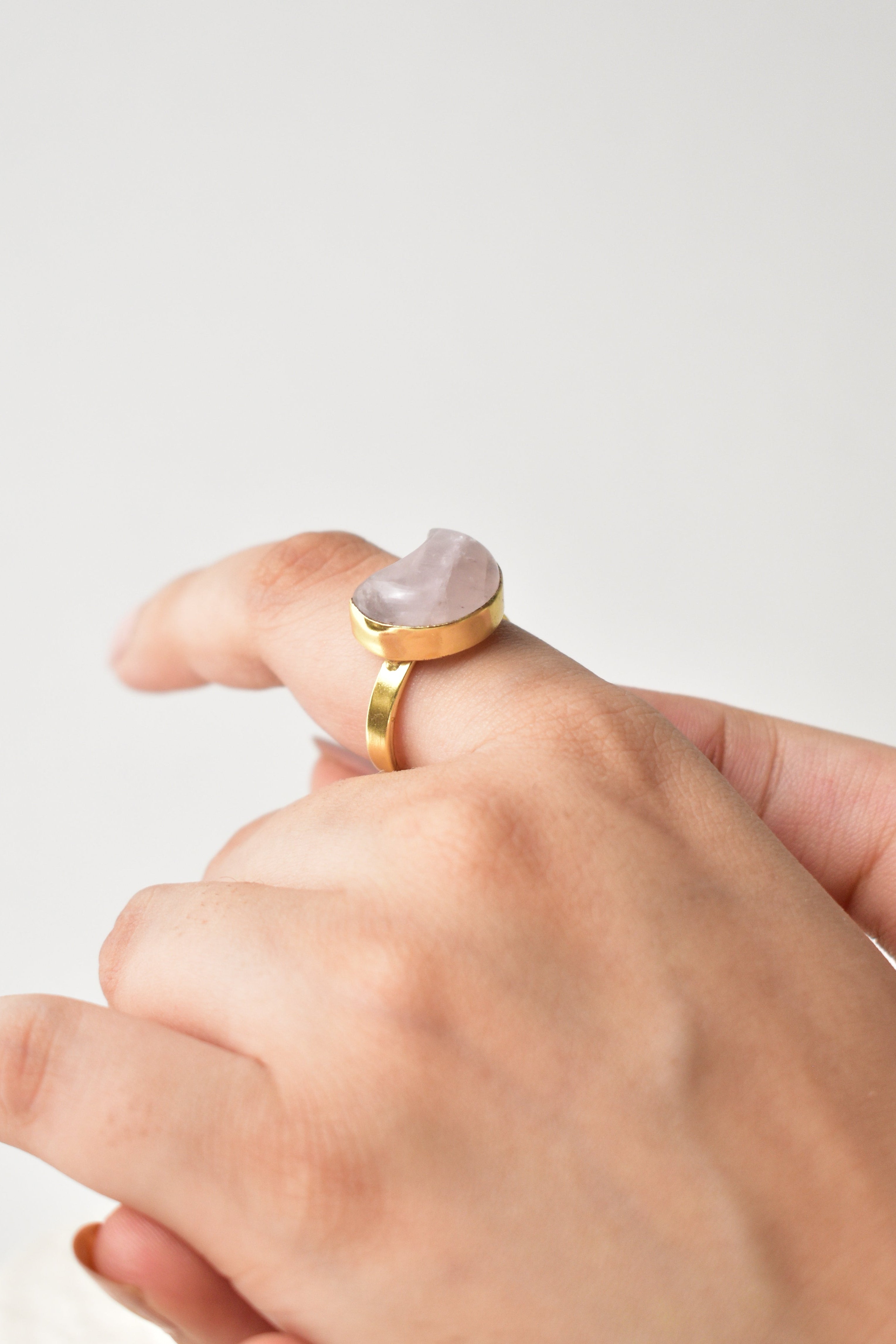 Hand wearing a gold ring with a heart-shaped pink stone on a light gray background Kokum jewels