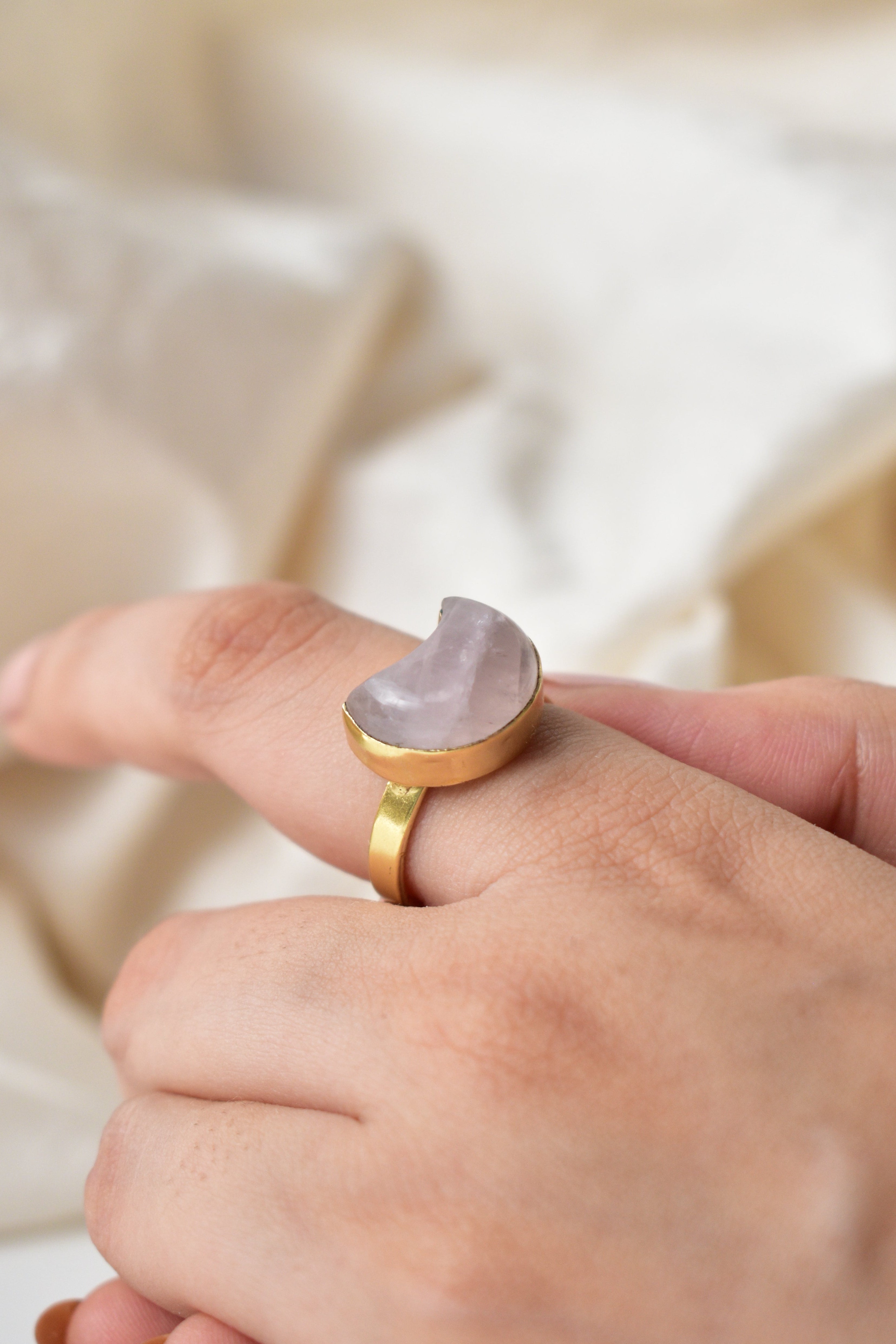 Hand wearing a gold ring with a pink stone on a blurred background Kokum jewels
