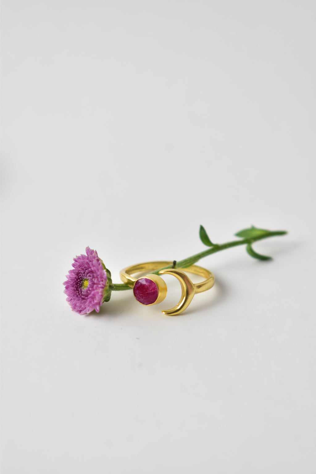 Gold earring with a red gemstone and flower on a white background