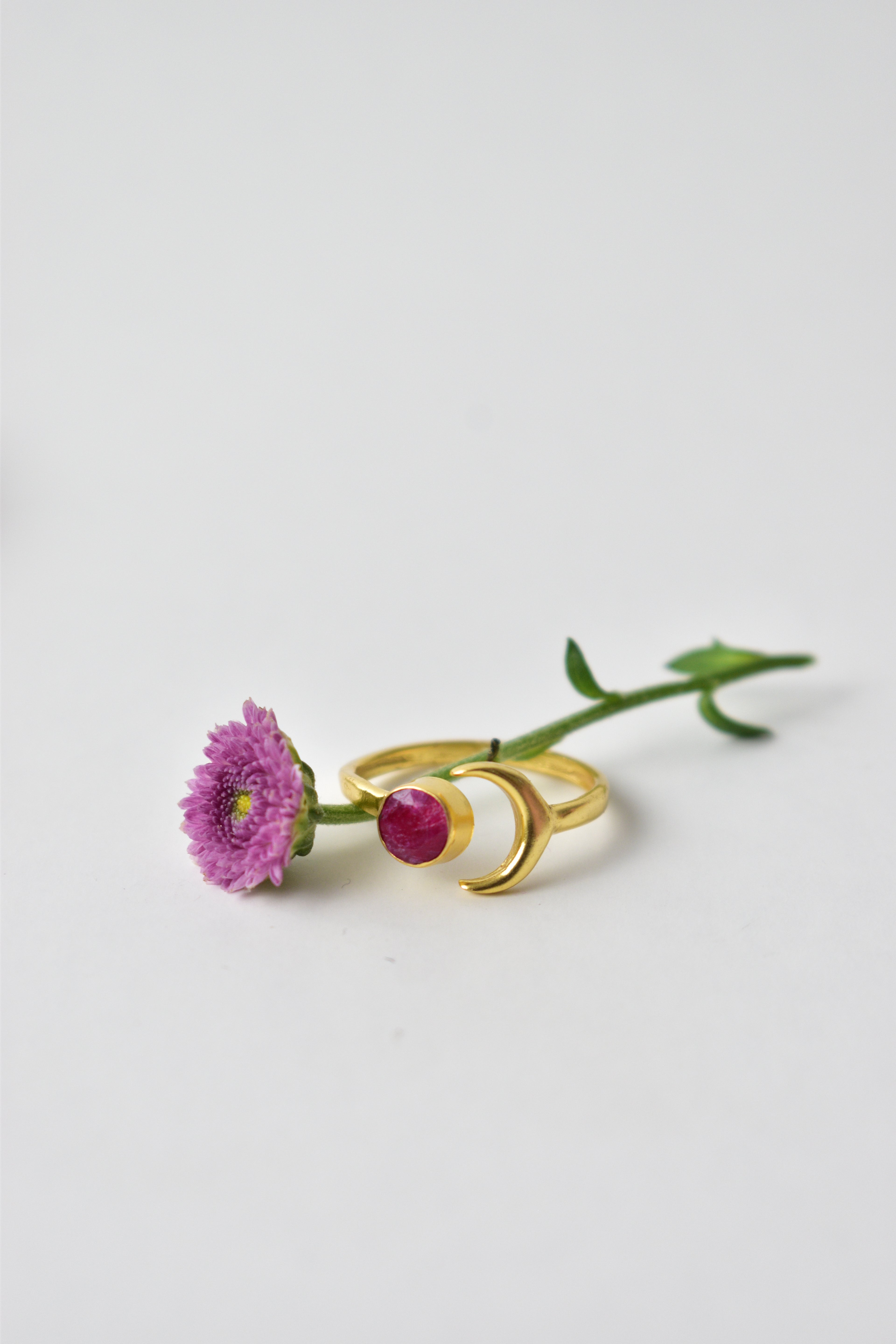 Gold earring with a red gemstone and flower on a white background