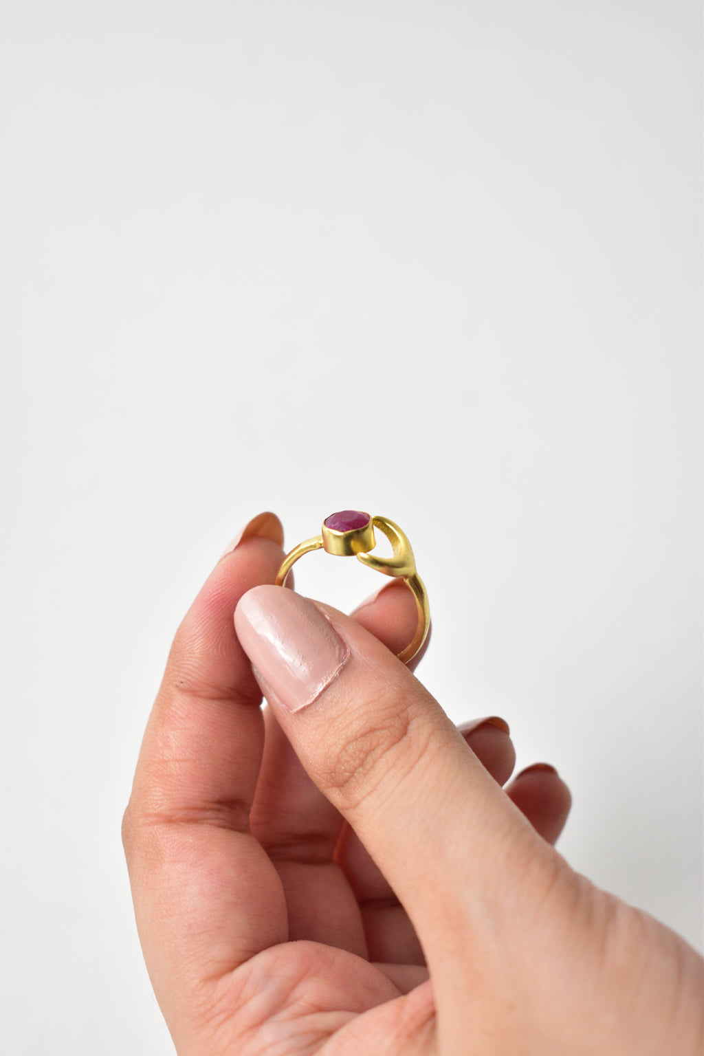 Gold ring with a purple gemstone held by a hand on a white background