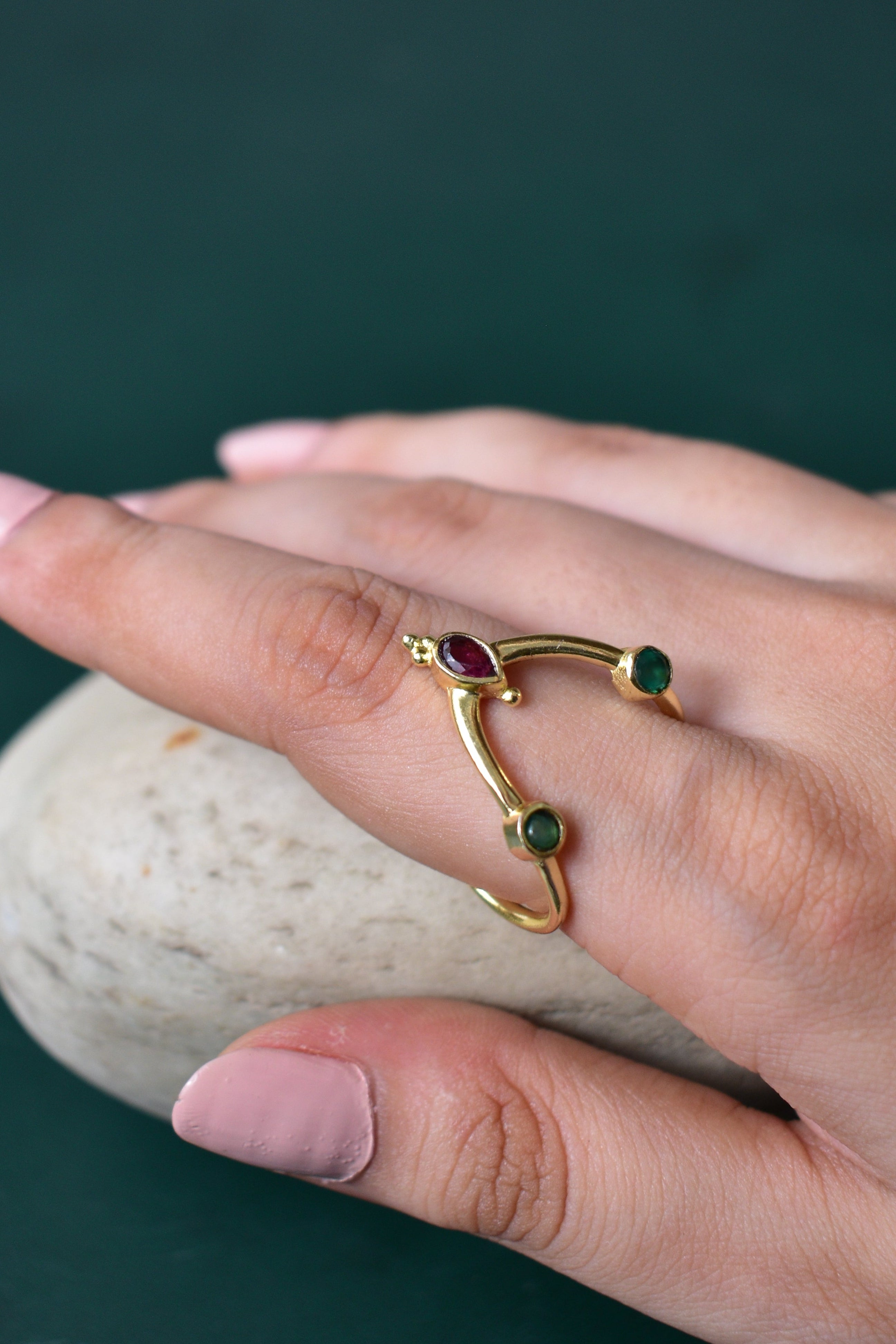 Gold ring with gemstones on a hand against a dark background