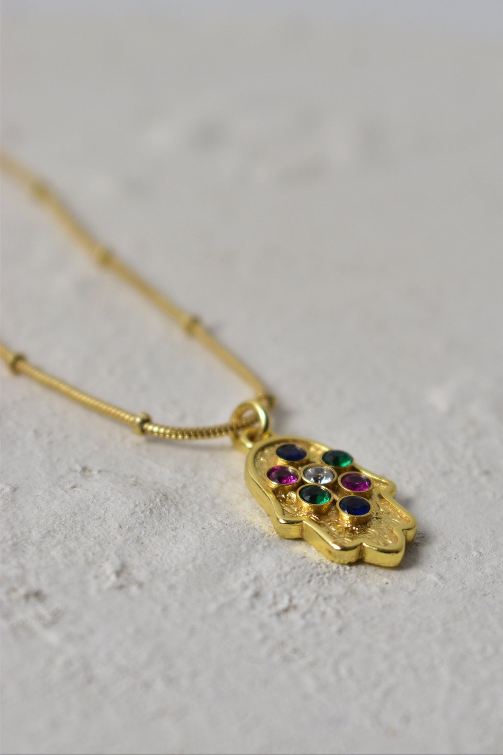 Gold snake-shaped earring with gemstones on a light gray background