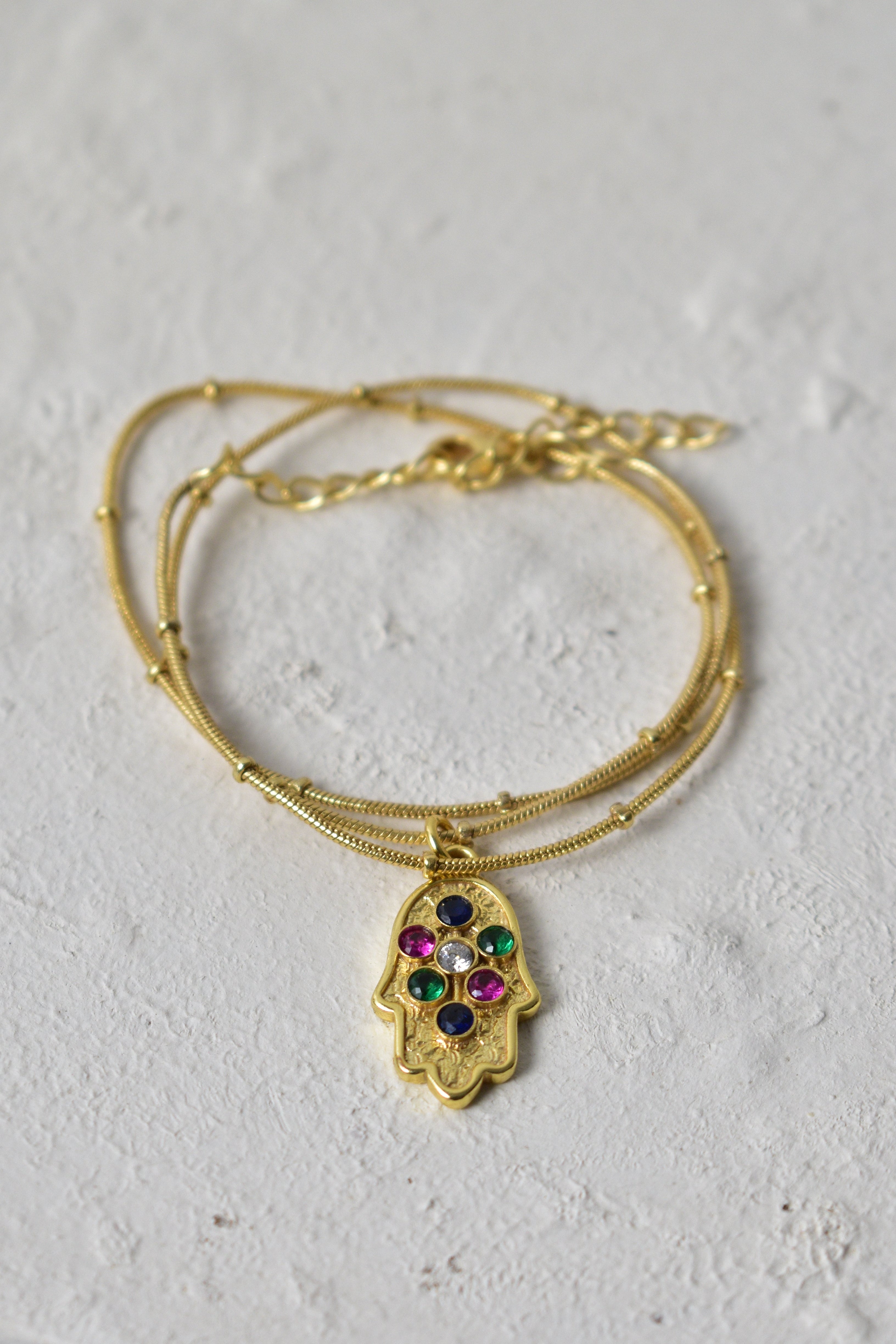 Gold bracelet with a hamsa hand charm on a textured white surface