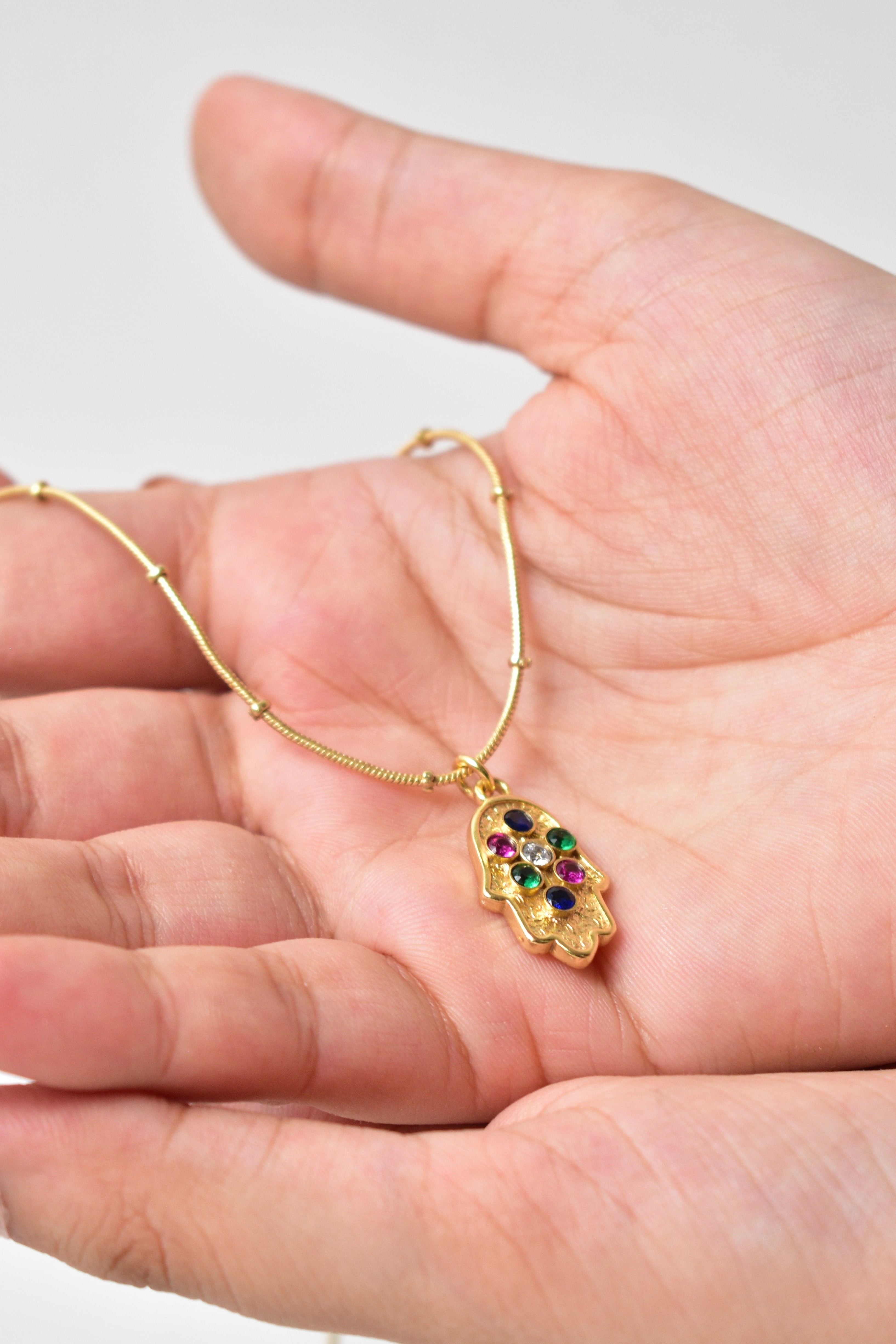 Gold bracelet with a colorful heart-shaped clasp held in a hand against a light background