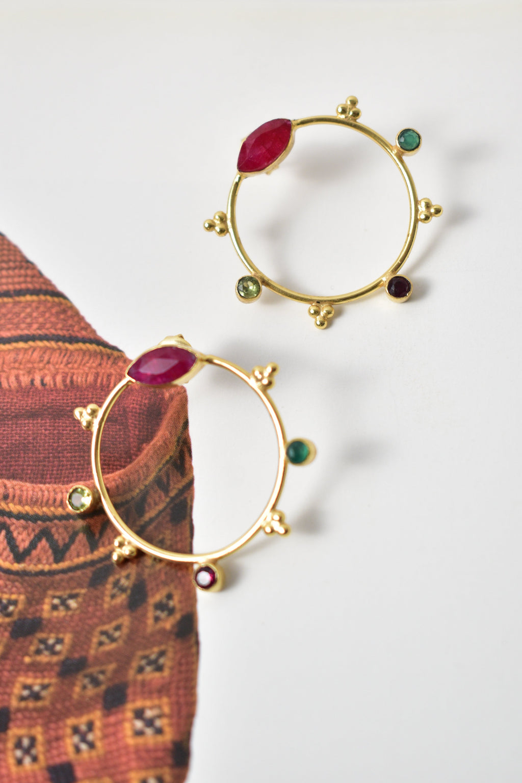 Gold hoop earrings with gemstones on a textured fabric background
