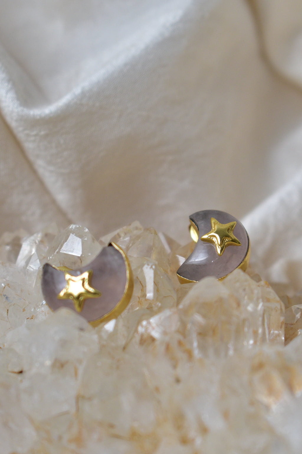 Pair of earrings with moon and star designs on a soft fabric background