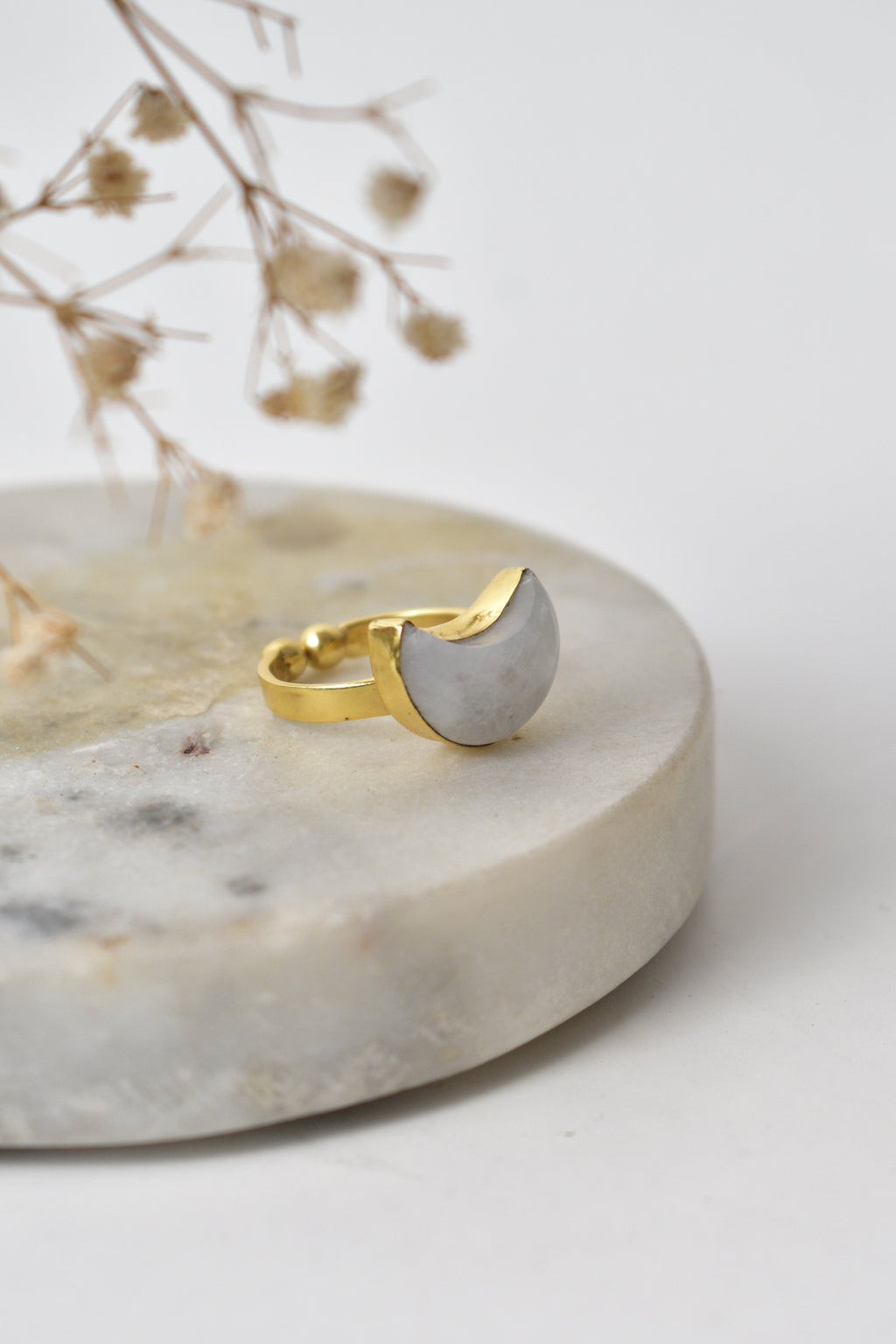 Gold and silver crescent moon-shaped earrings on a marble surface with dried flowers. Kokum jewels
