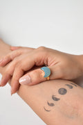 Two hands holding each other with a visible tattoo on the arm against a light background