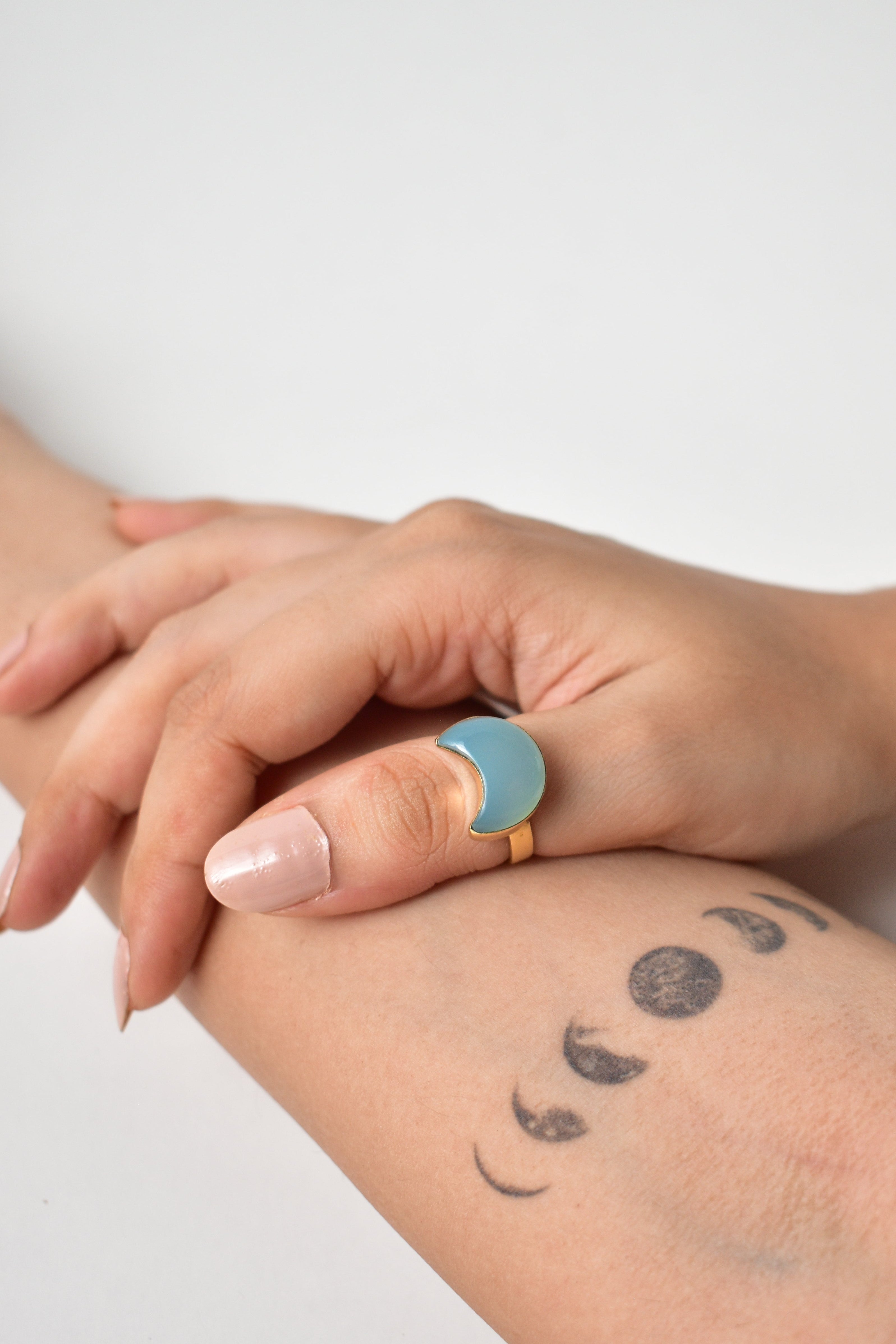 Two hands holding each other with a visible tattoo on the arm against a light background