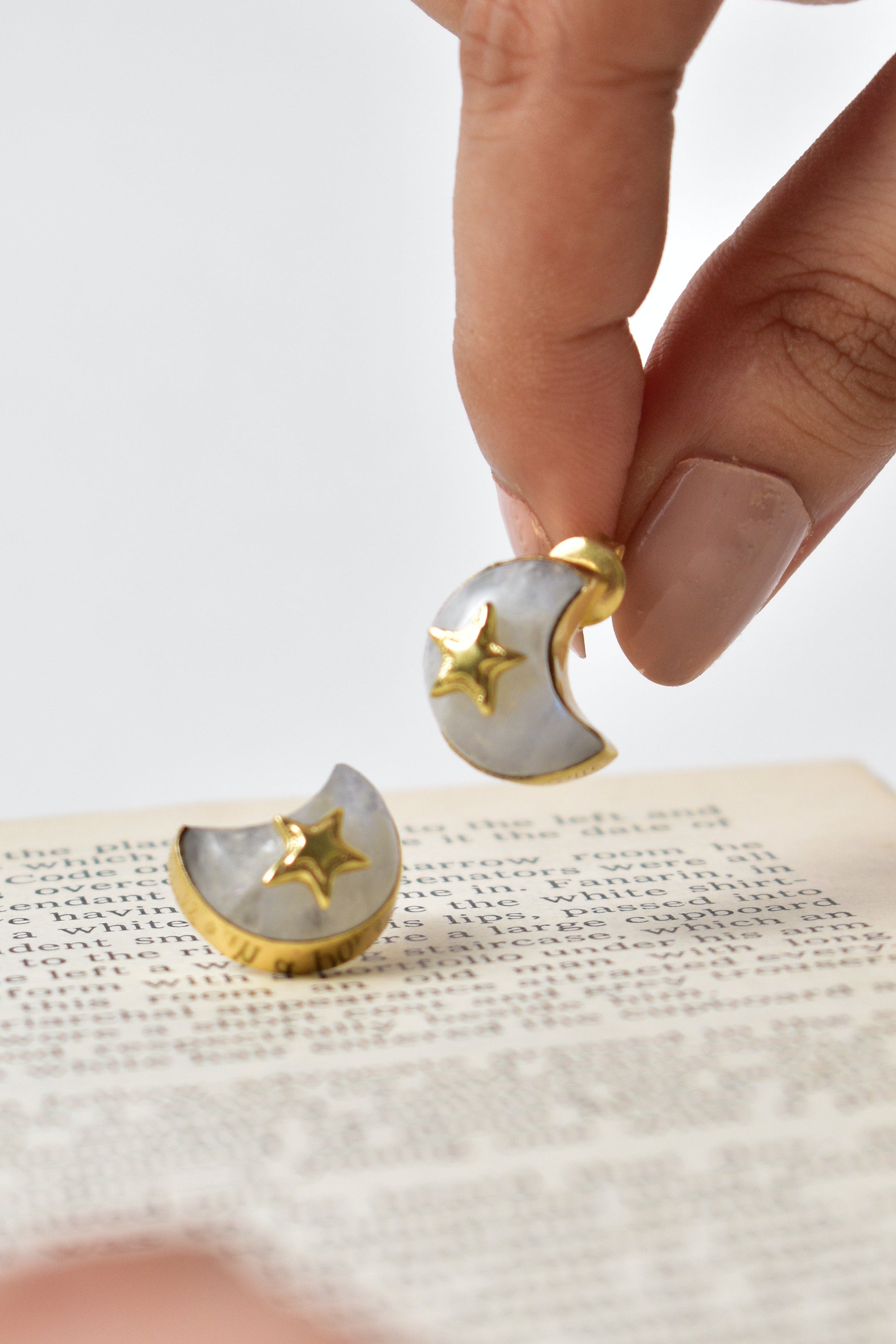 Person holding a small gold and white earring against a neutral background