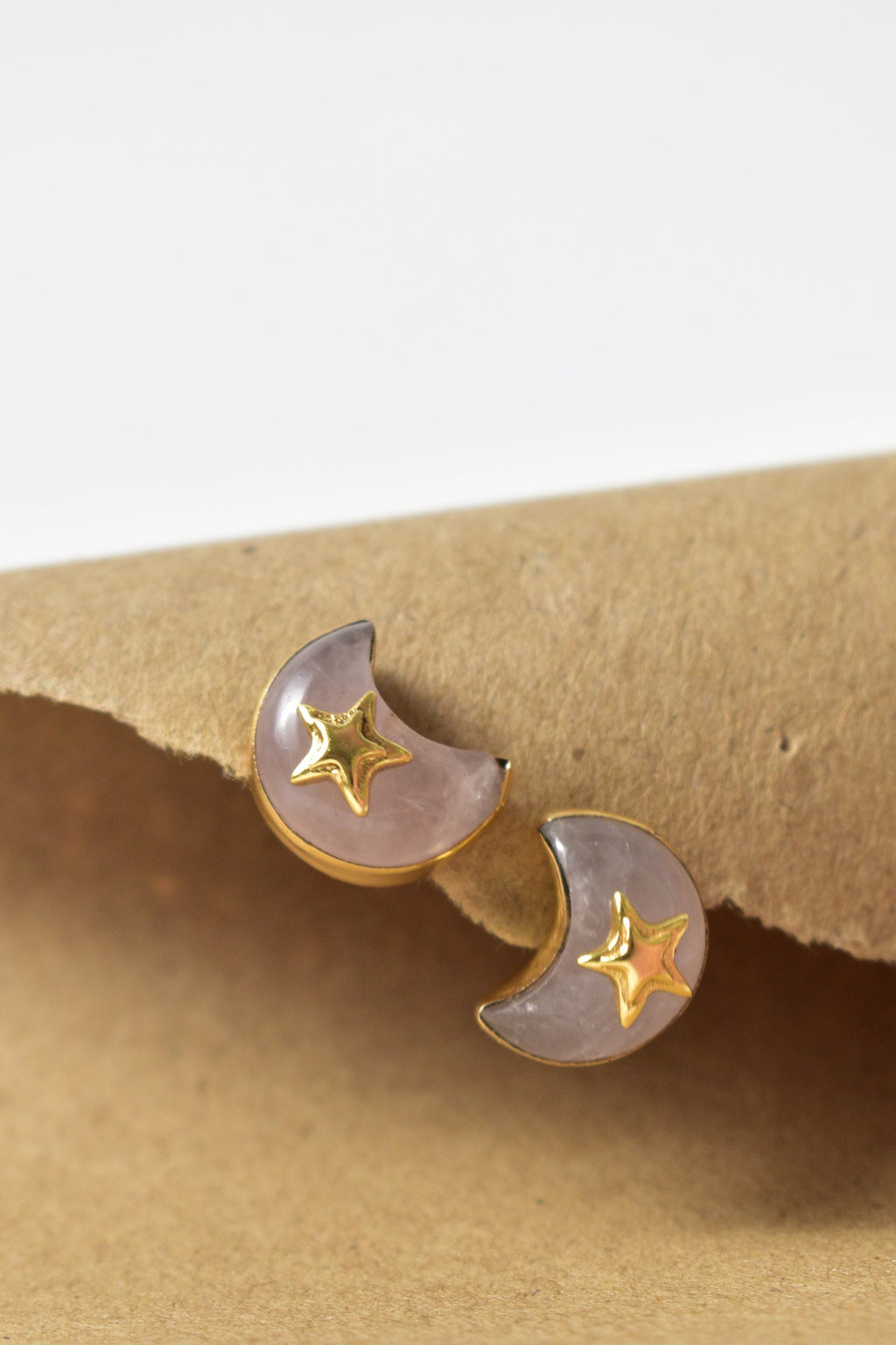 Pair of moon and star earrings on a beige earring stand with a white background