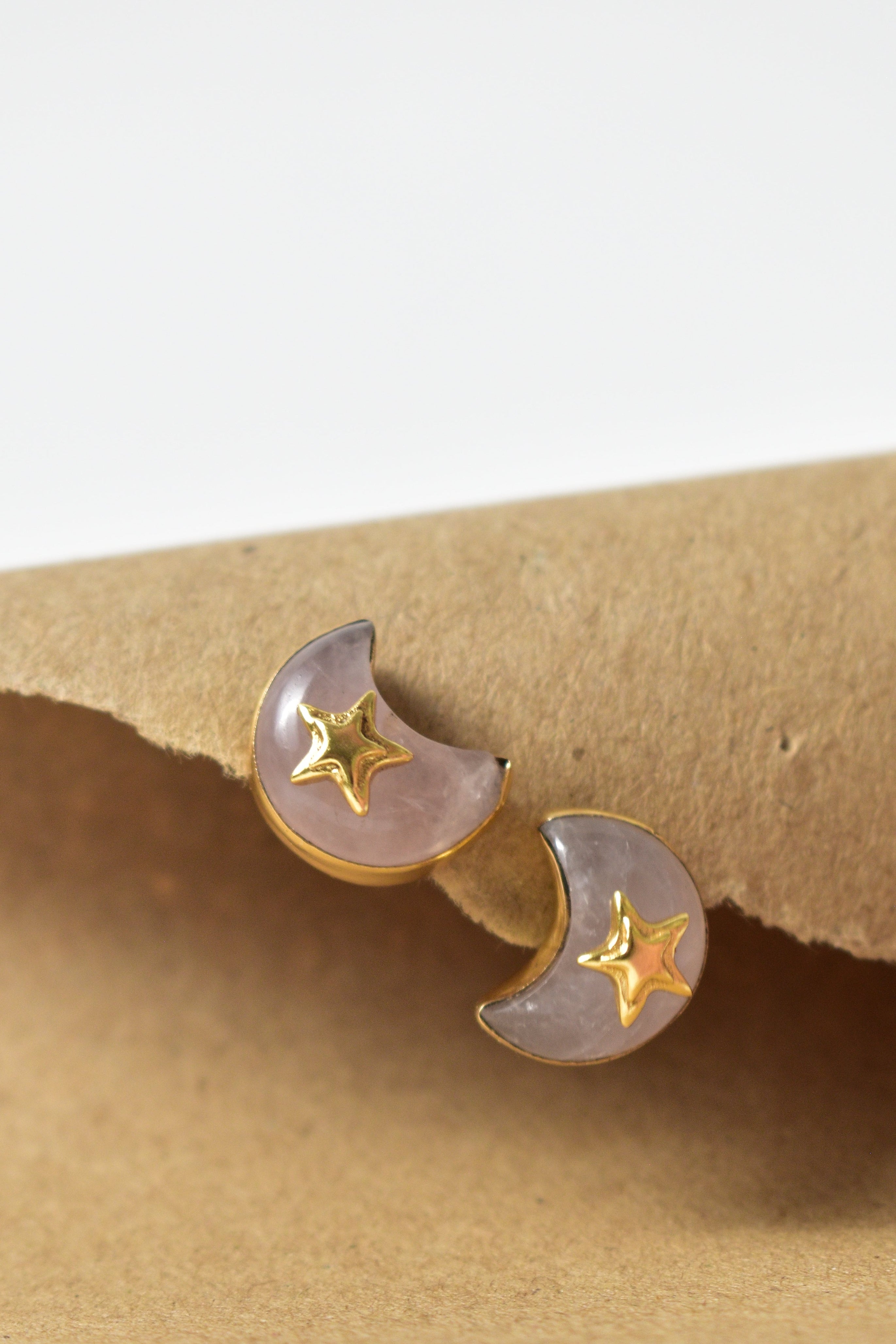 Pair of moon and star earrings on a beige earring stand with a white background