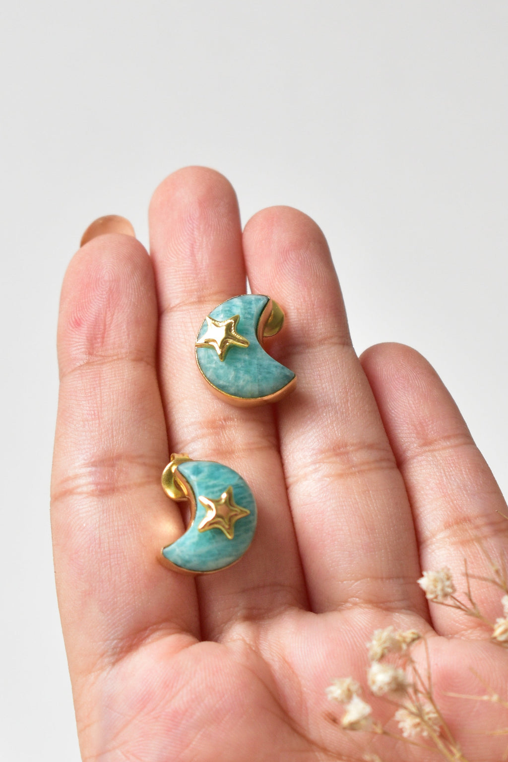 Hand holding a pair of turquoise earrings with gold accents on a light gray background