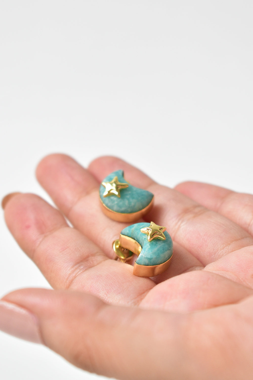 Hand holding turquoise earrings with gold accents against a light background