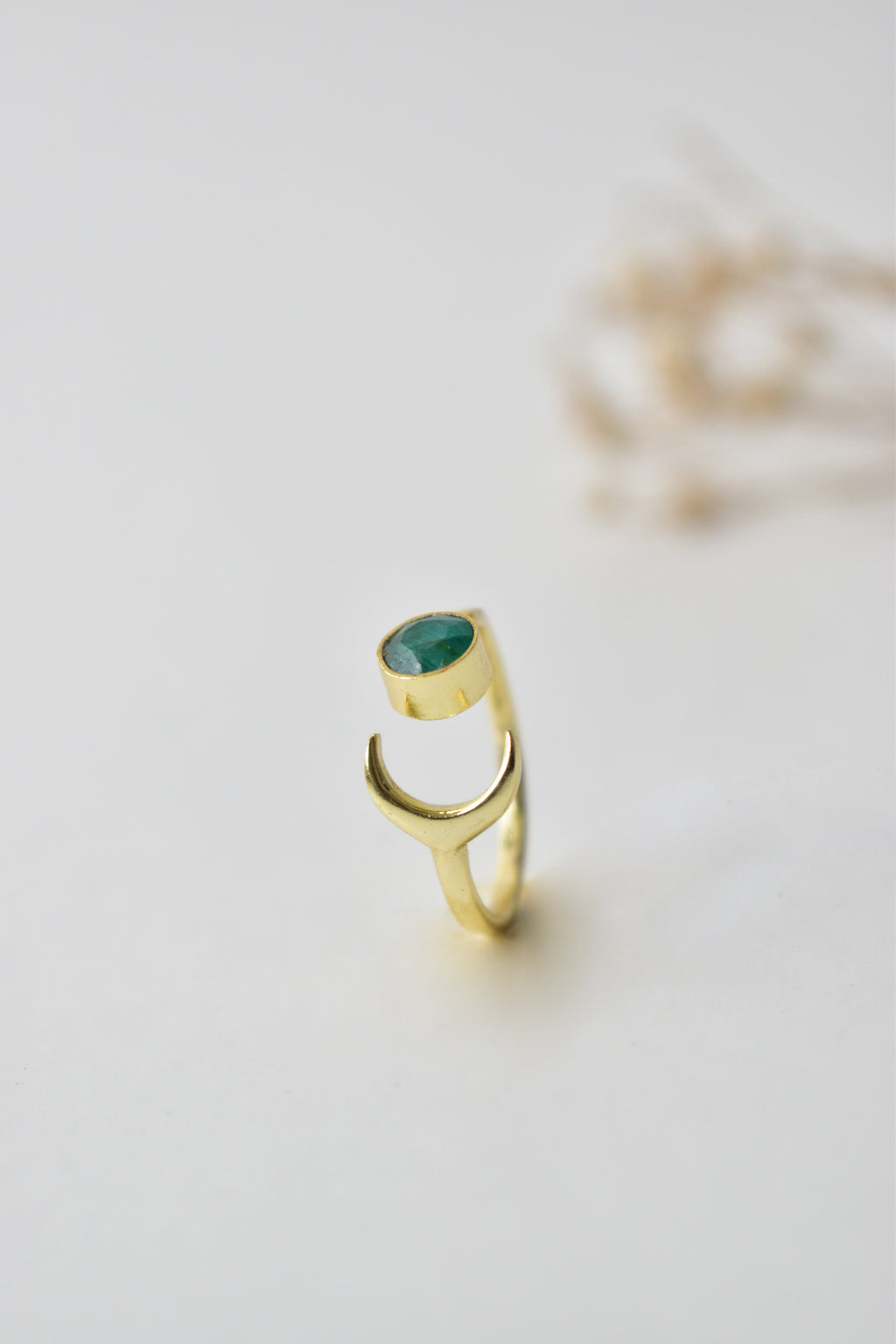 Gold ring with a green gemstone on a light gray background
