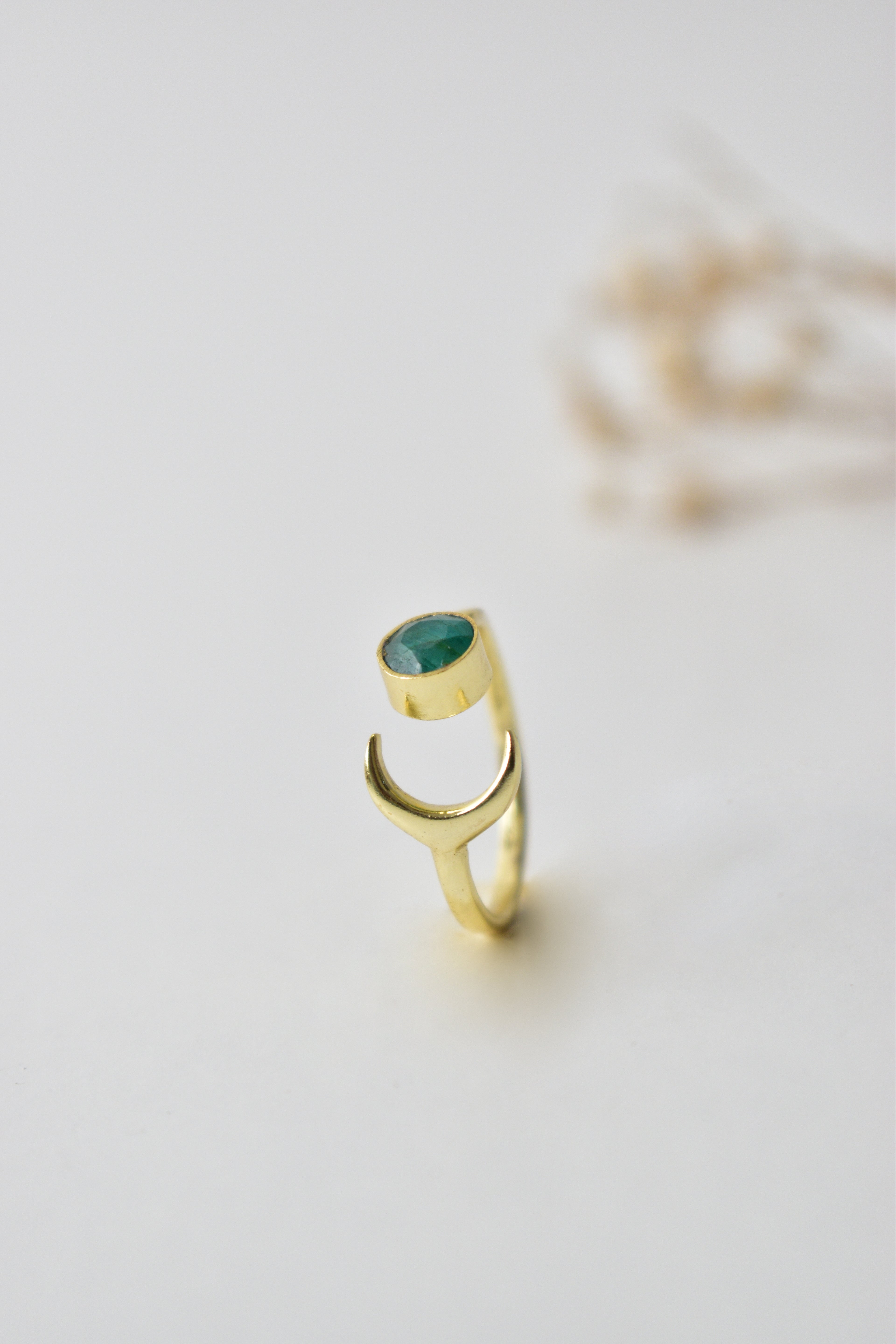 Gold ring with a green gemstone on a light gray background