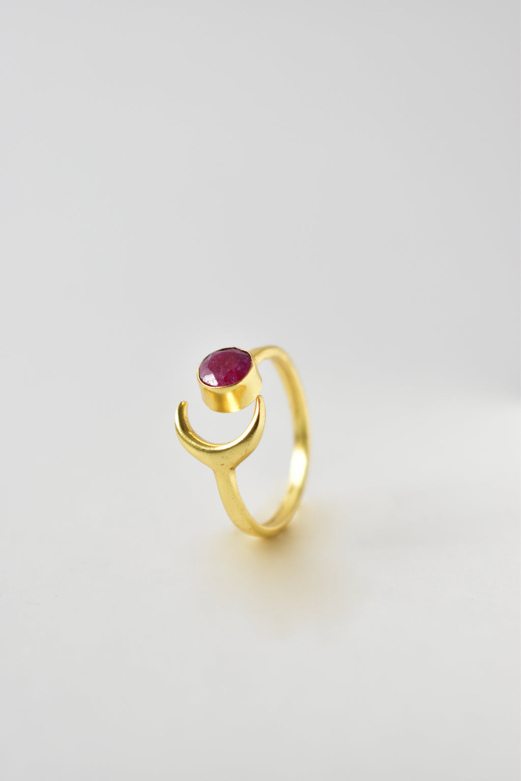 Gold ring with a red gemstone on a light gray background