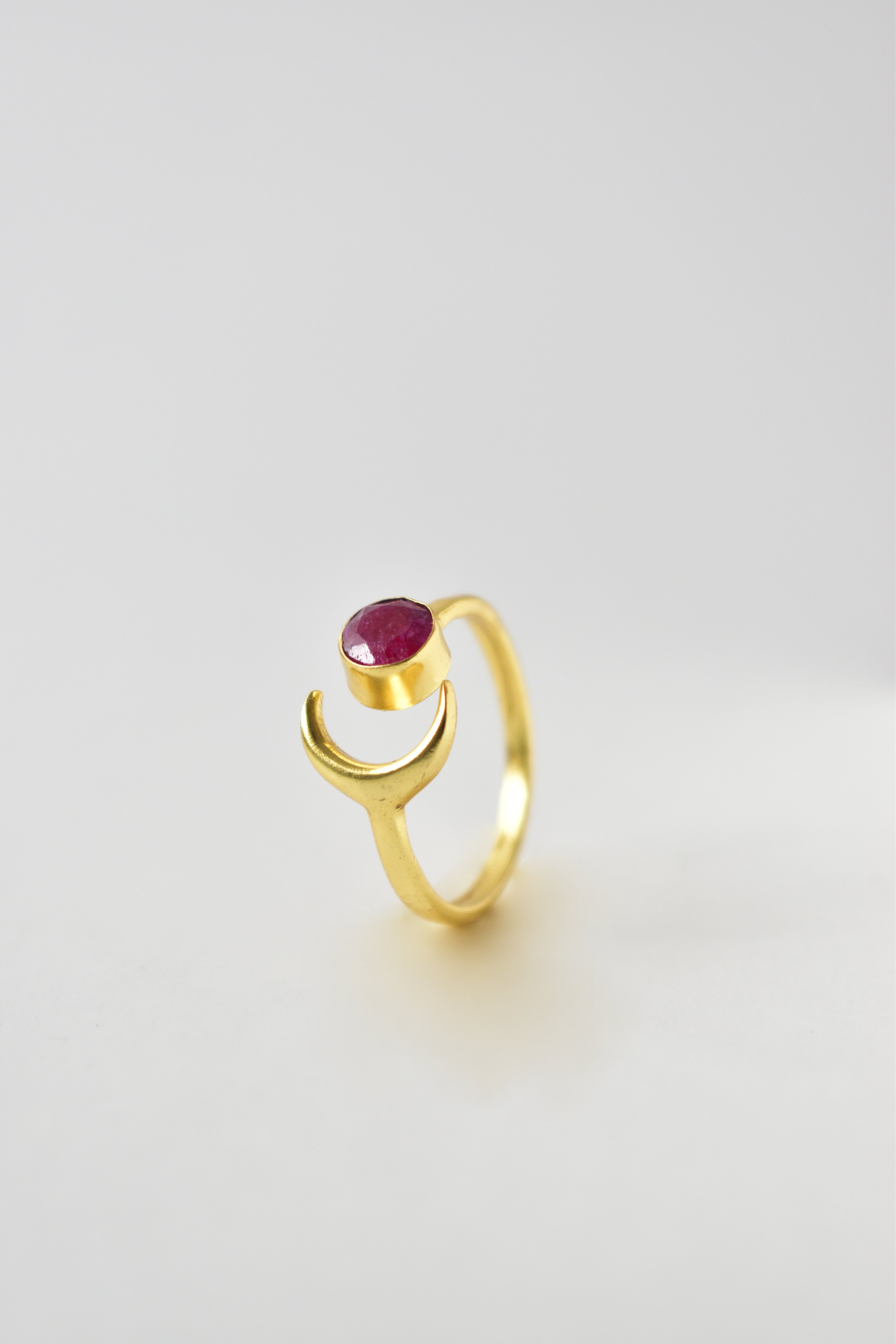 Gold ring with a red gemstone on a light gray background